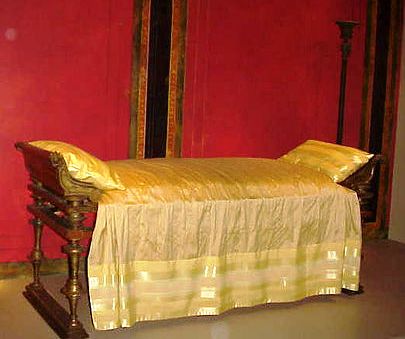 Ancient bed with gold covering and background wall painted dark red